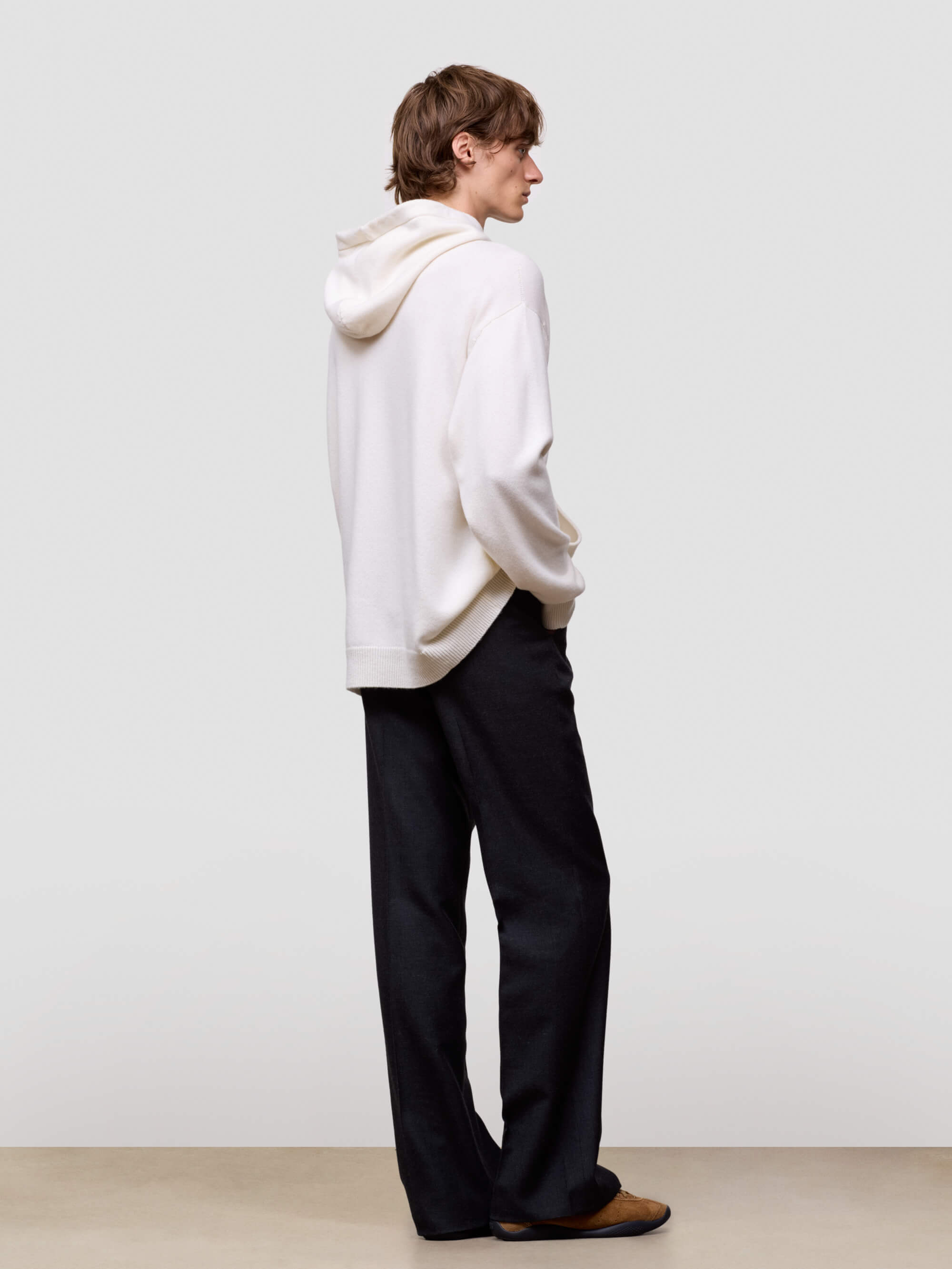 man wearing a white cashmere hoodie and black pants on a light gray background