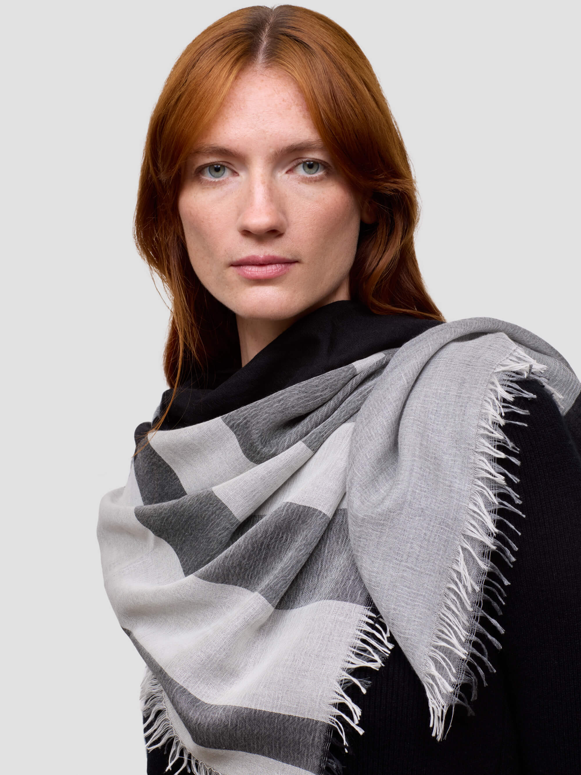 Woman wearing a gray and white patterned scarf on a plain background