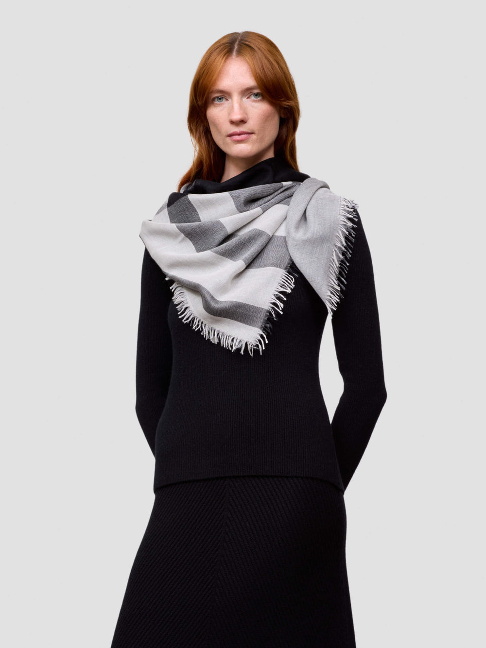 Woman wearing a black outfit with a gray and white checkered scarf on a light gray background