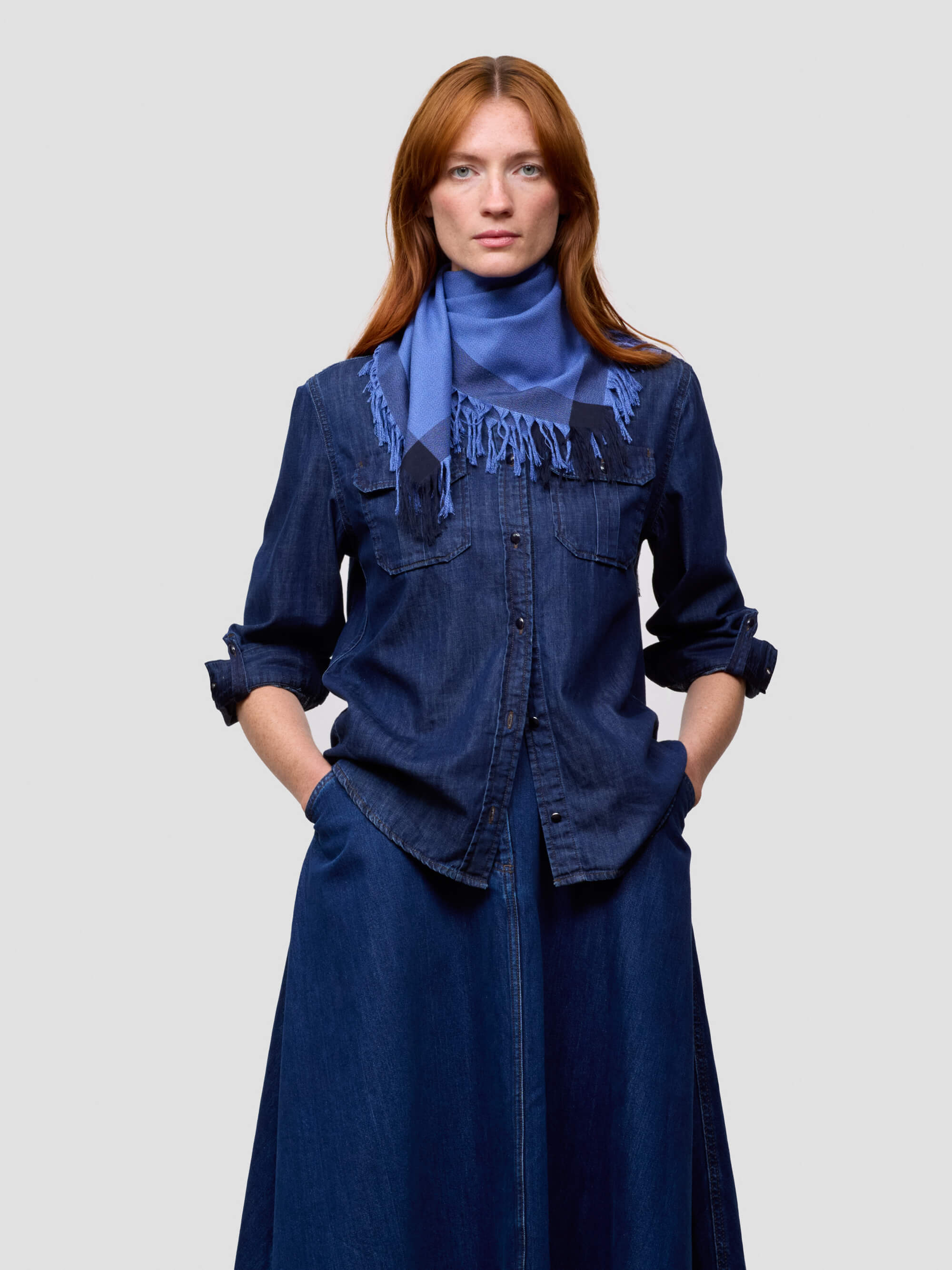 Woman wearing a blue denim outfit with a blue scarf on a light gray background