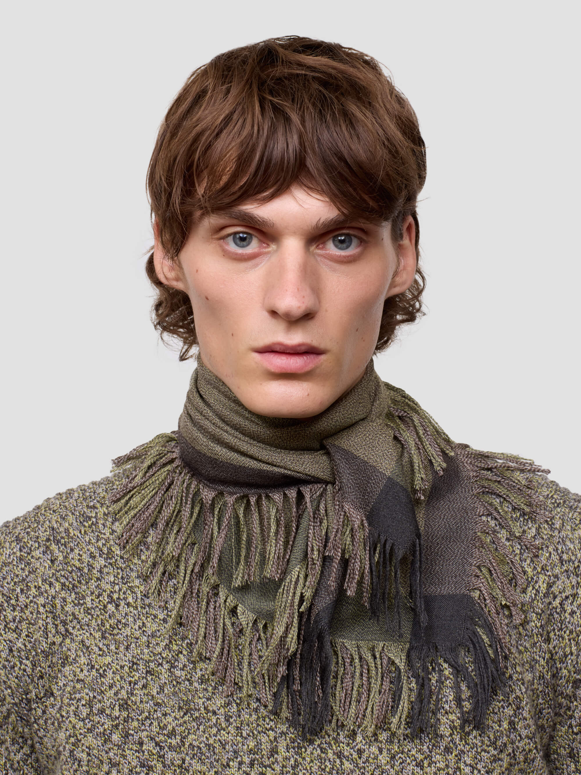 Man wearing a green cashmere scarf and patterned cashmere sweater against a light gray background