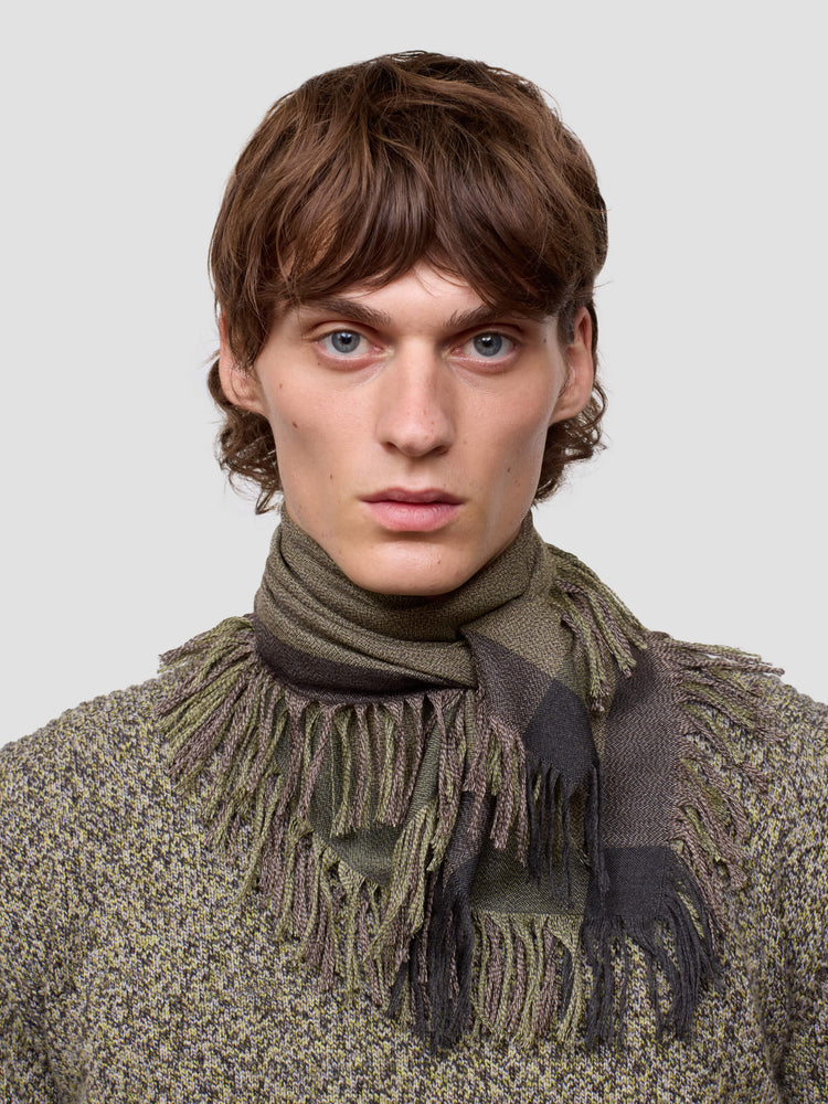 Man wearing a green cashmere scarf and patterned cashmere sweater against a light gray background
