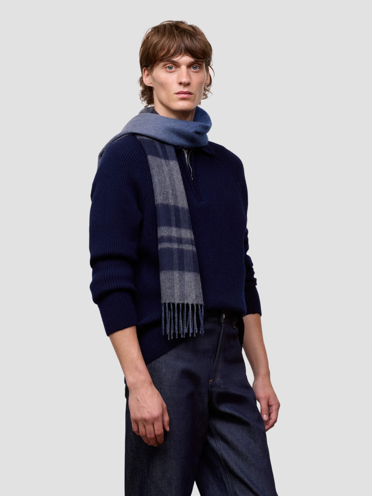 Man wearing a dark blue cashmere sweater and plaid cashmere scarf against a light gray background