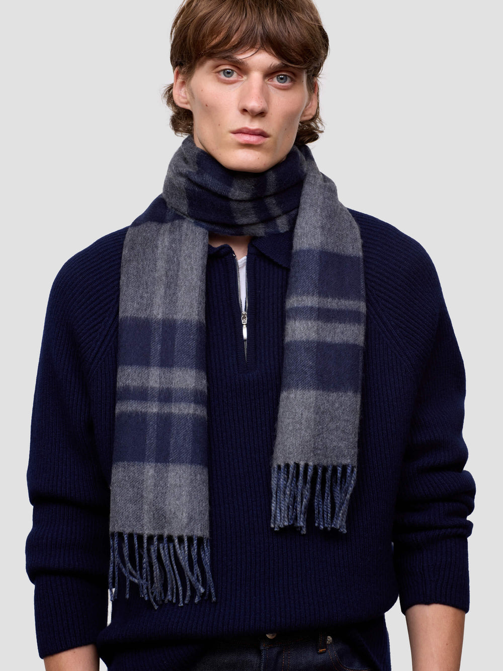 Man wearing a dark blue cashmere sweater and plaid cashmere scarf against a light gray background