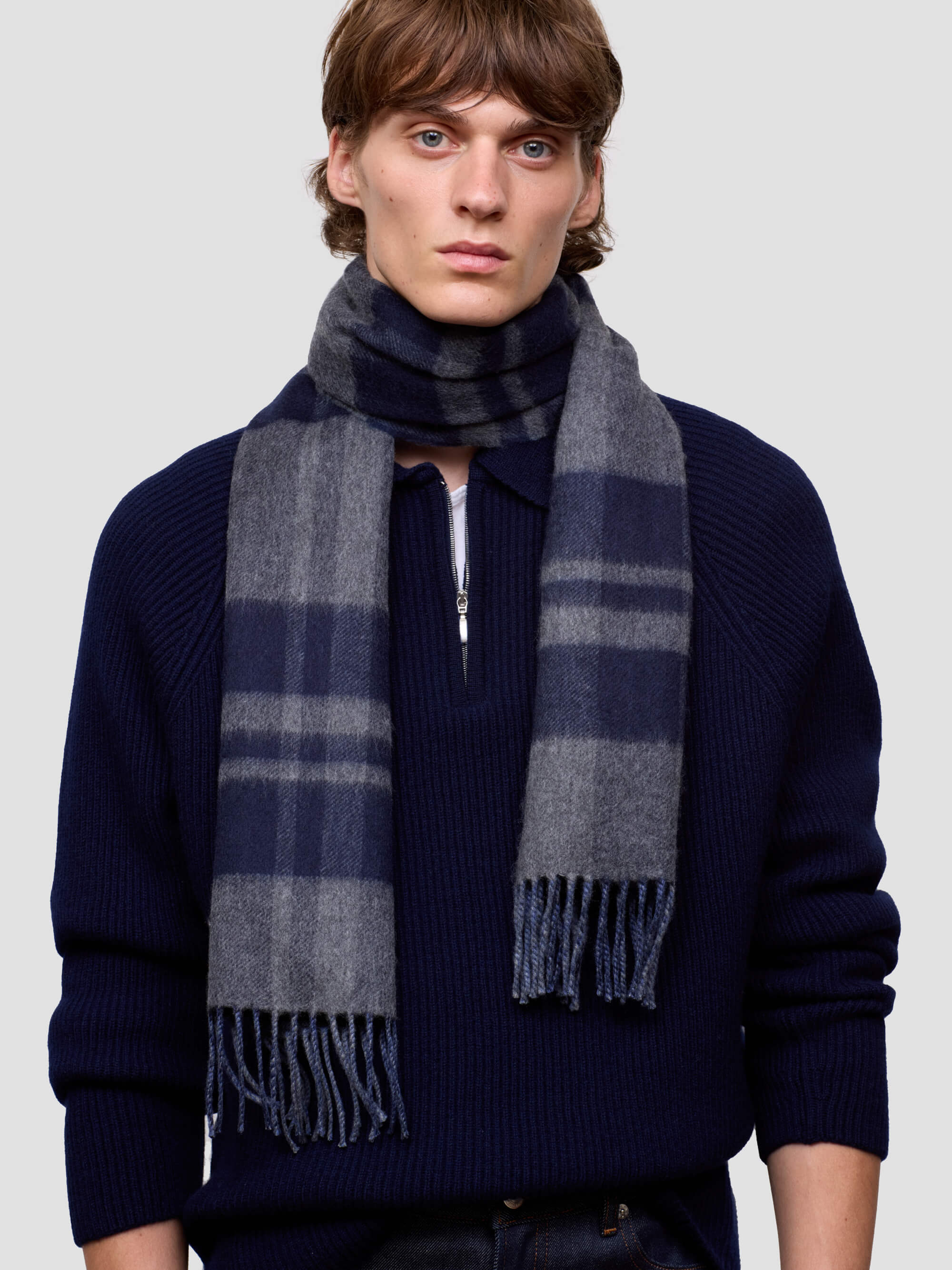 Man wearing a dark blue cashmere sweater and plaid cashmere scarf against a light gray background