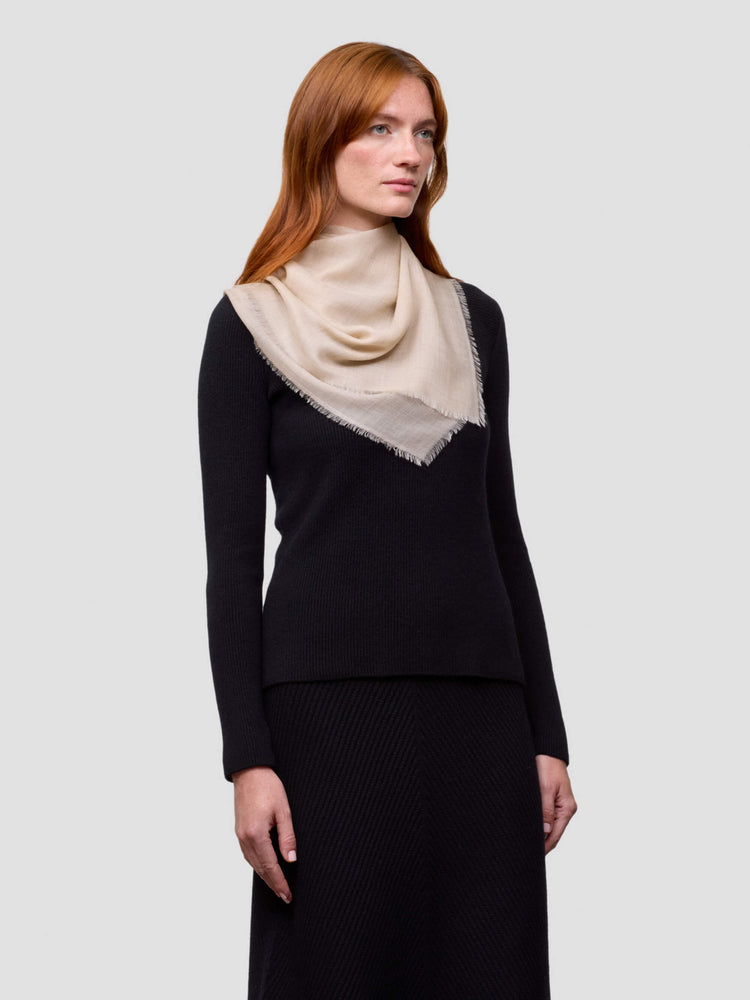 Woman wearing a black cashmere sweater with a beige square cashmere scarf on a light gray background