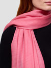 Woman wearing a black cashmere dress and pink cashmere scarf on a white background
