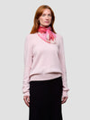 Woman wearing a light pink sweater and black skirt with a pink scarf on a white background