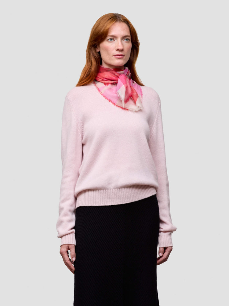 Woman wearing a light pink sweater and black skirt with a pink scarf on a white background