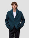 Man wearing a green cashmere cardigan over a white shirt on a light gray background