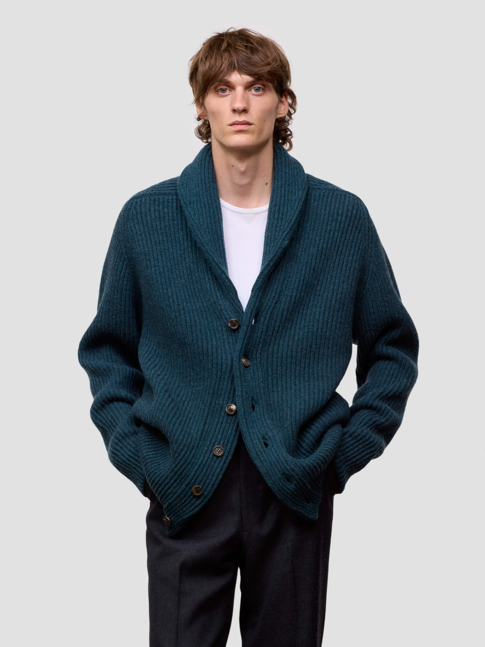 Man wearing a green cashmere cardigan over a white shirt on a light gray background