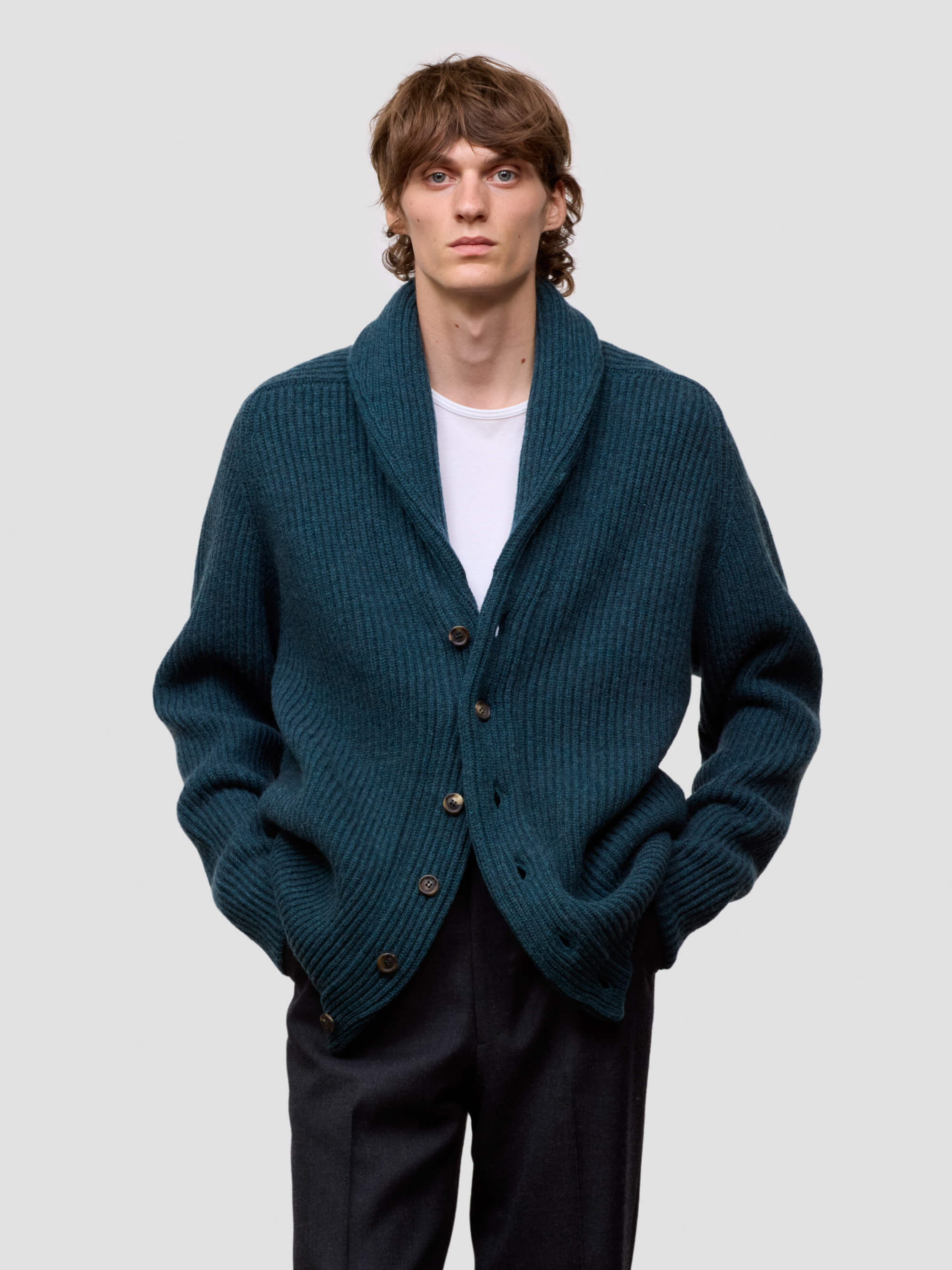 Man wearing a green cashmere cardigan over a white shirt on a light gray background