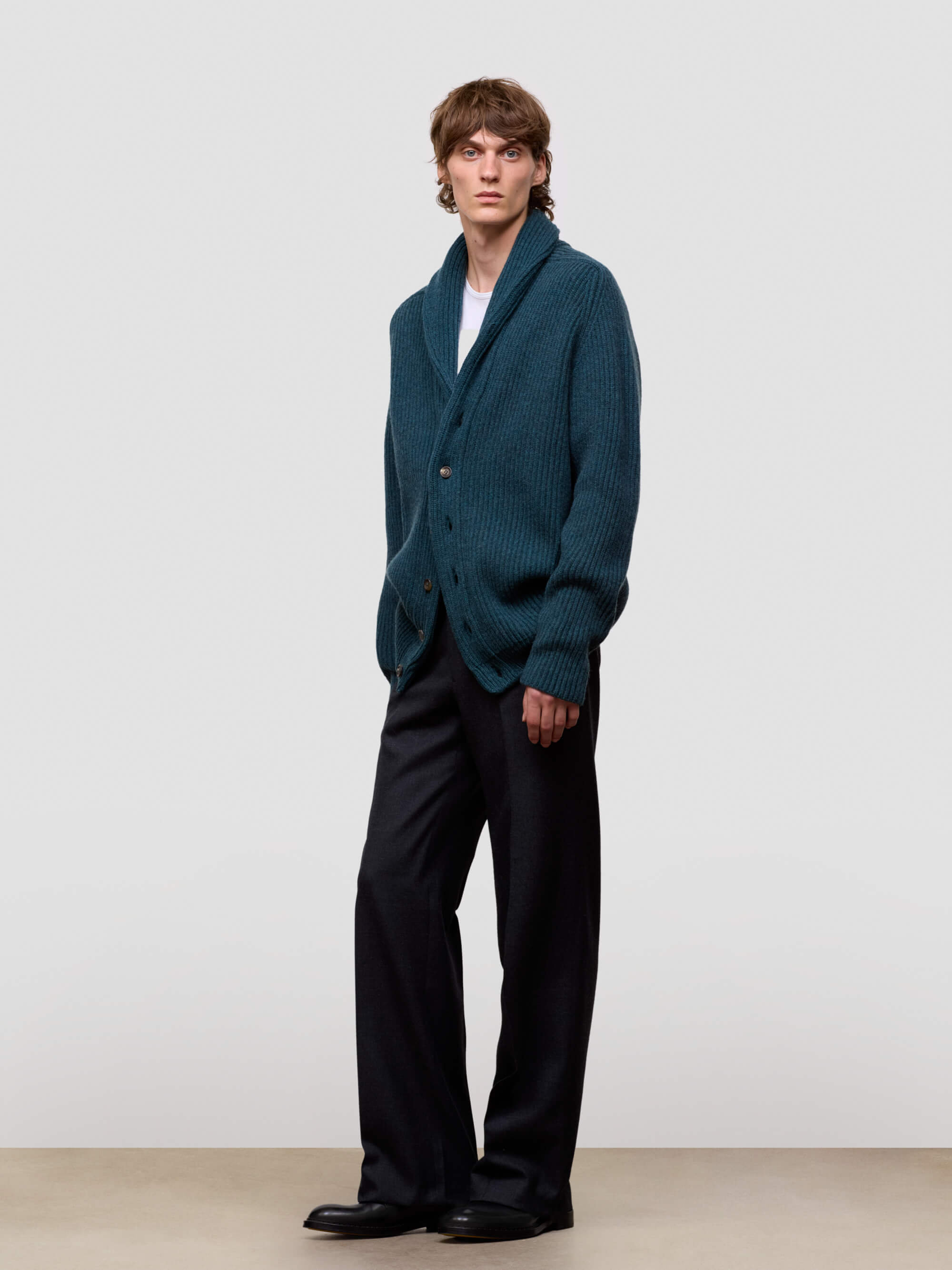 Man wearing a green cashmere cardigan over a white shirt on a light gray background