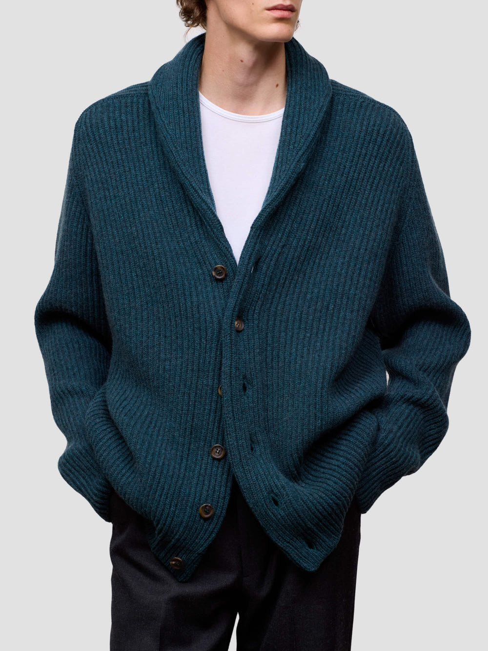 Man wearing a green cashmere cardigan over a white shirt on a light gray background