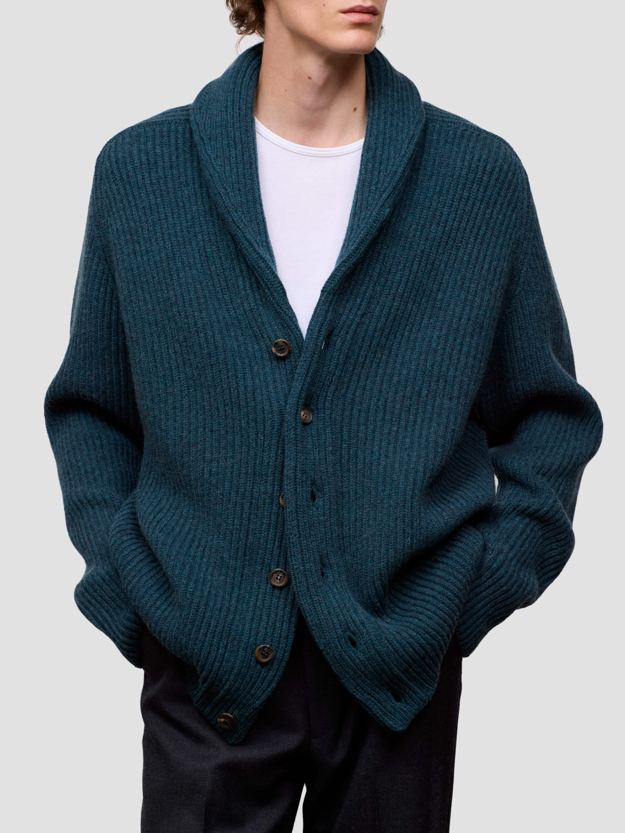 Man wearing a green cashmere cardigan over a white shirt on a light gray background