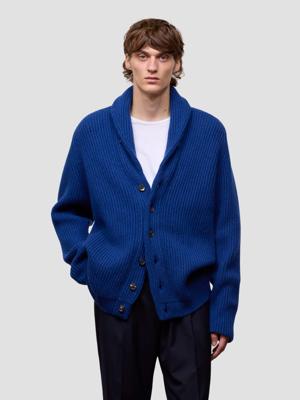 man wearing a blue cashmere cardigan over a white shirt on a light gray background