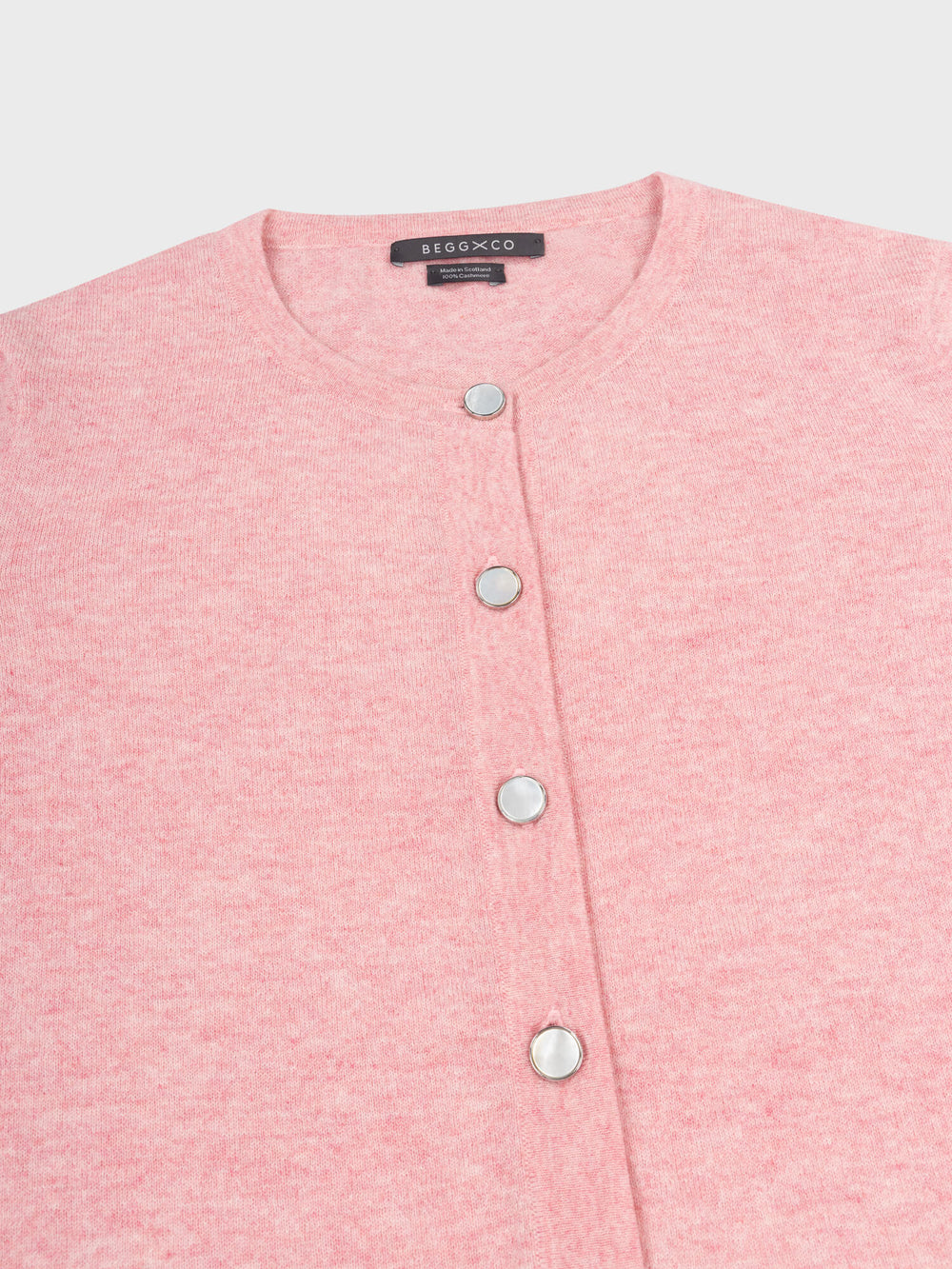 close up of a pink cashmere cardigan with pearl buttons on a grey background