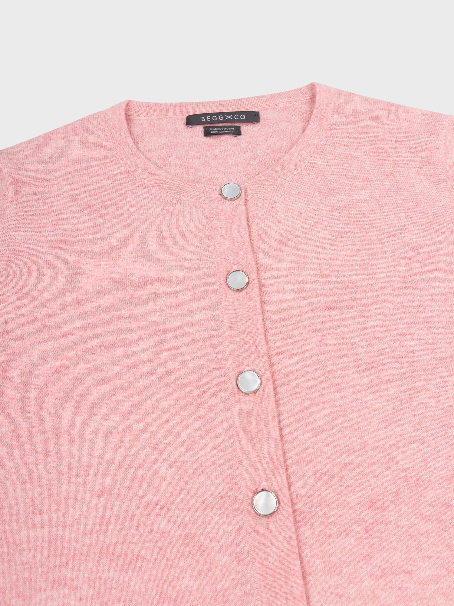 close up of a pink cashmere cardigan with pearl buttons on a grey background