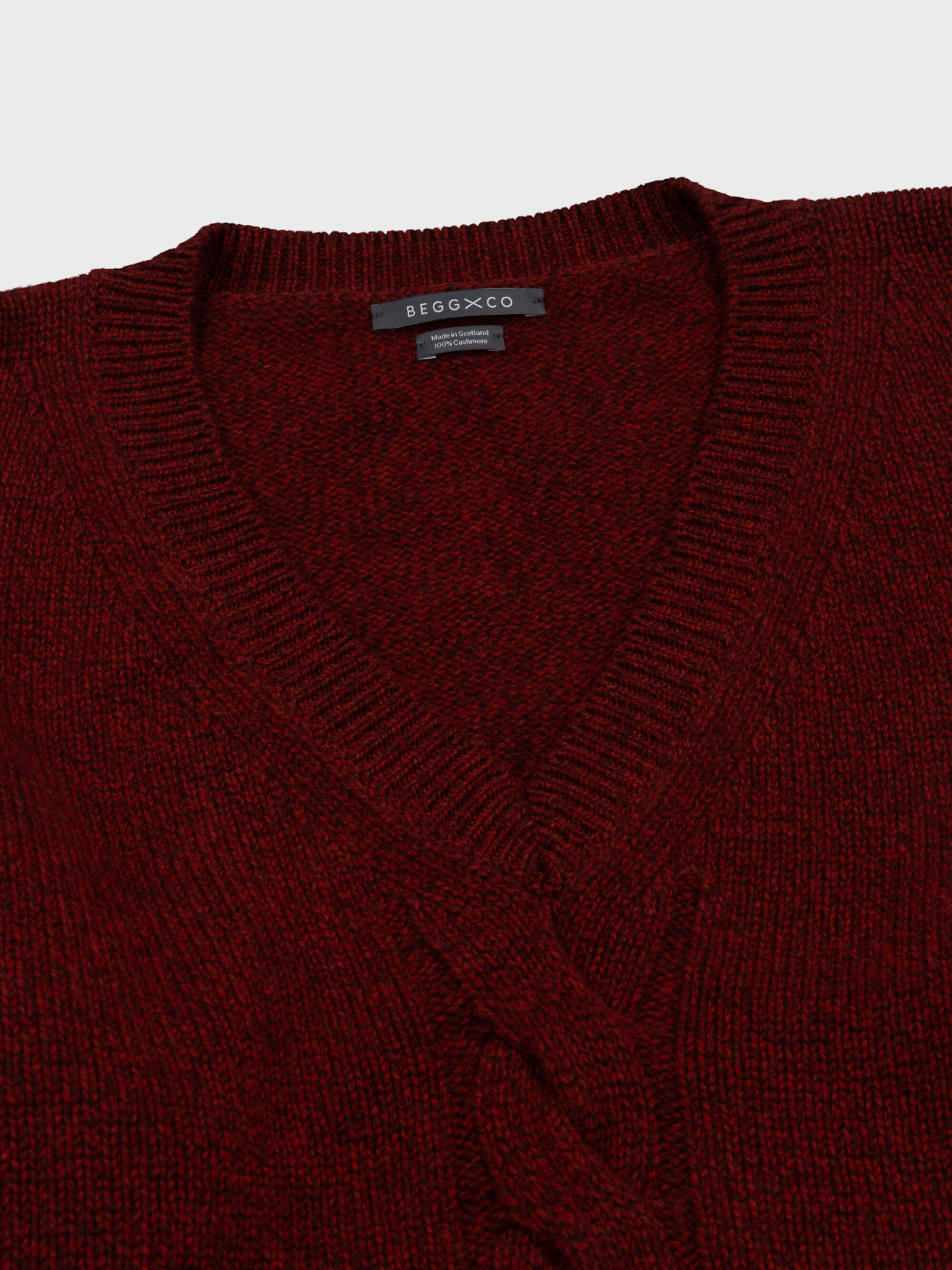 red cashmere v-neck sweater detail with cable knit detail down middle on grey background
