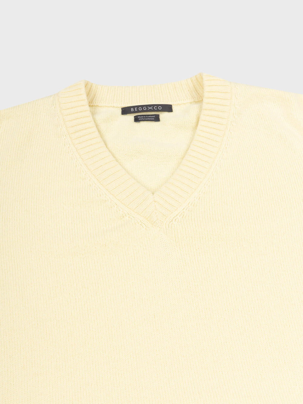 close up of a light yellow v-neck sweater on a grey background