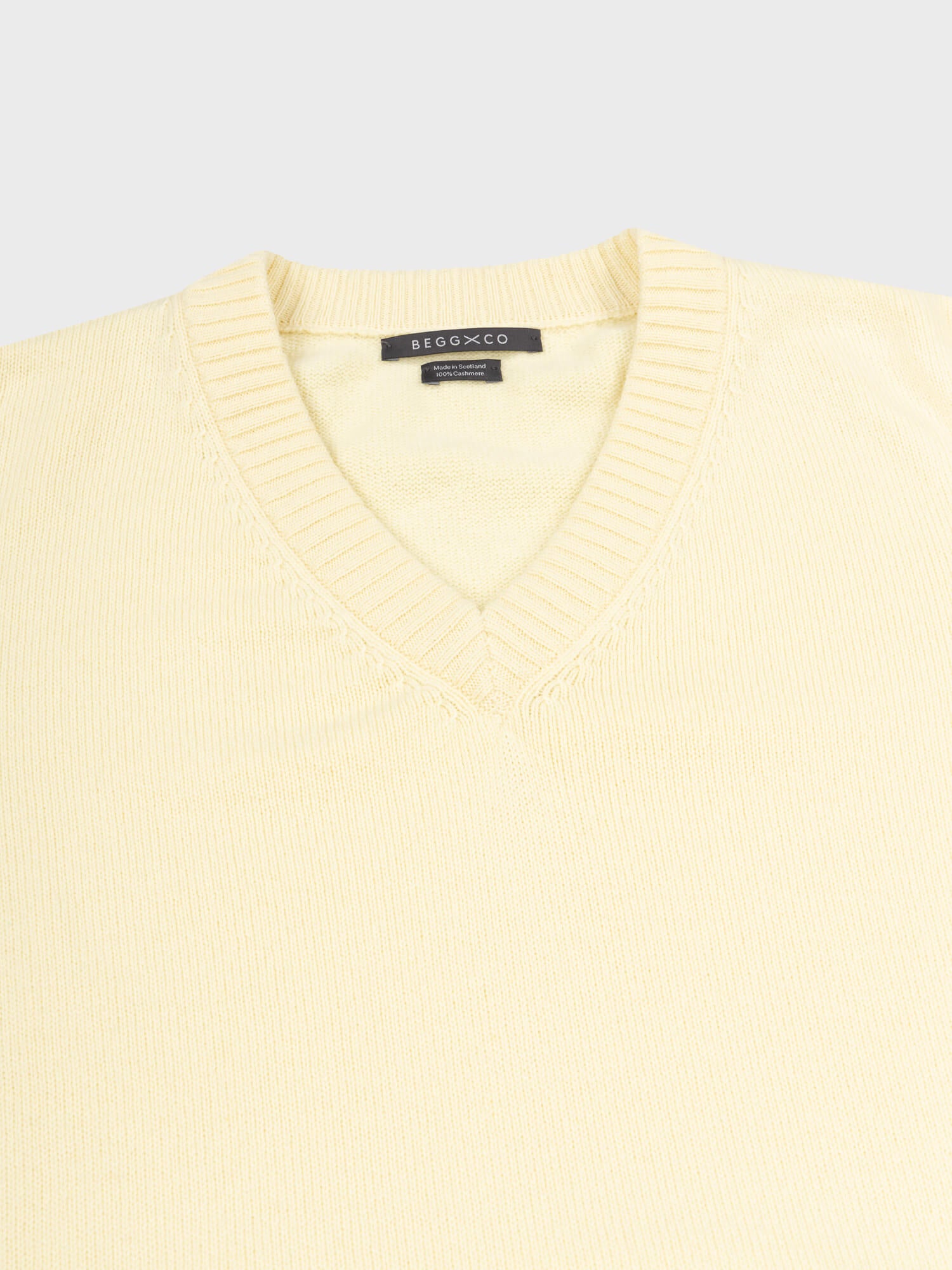 close up of a light yellow v-neck sweater on a grey background