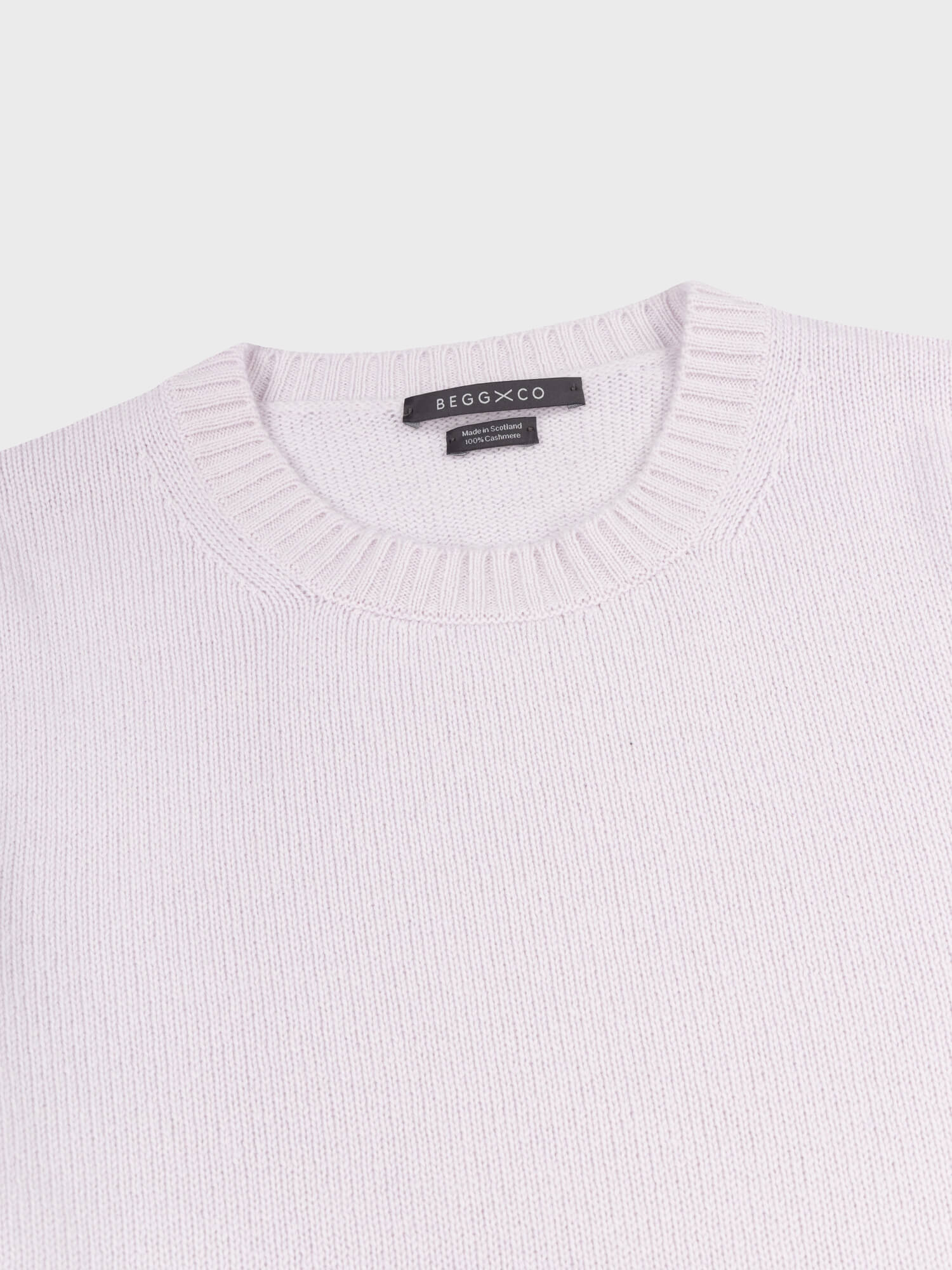 crewneck detail of a light purple cashmere sweater on a grey background