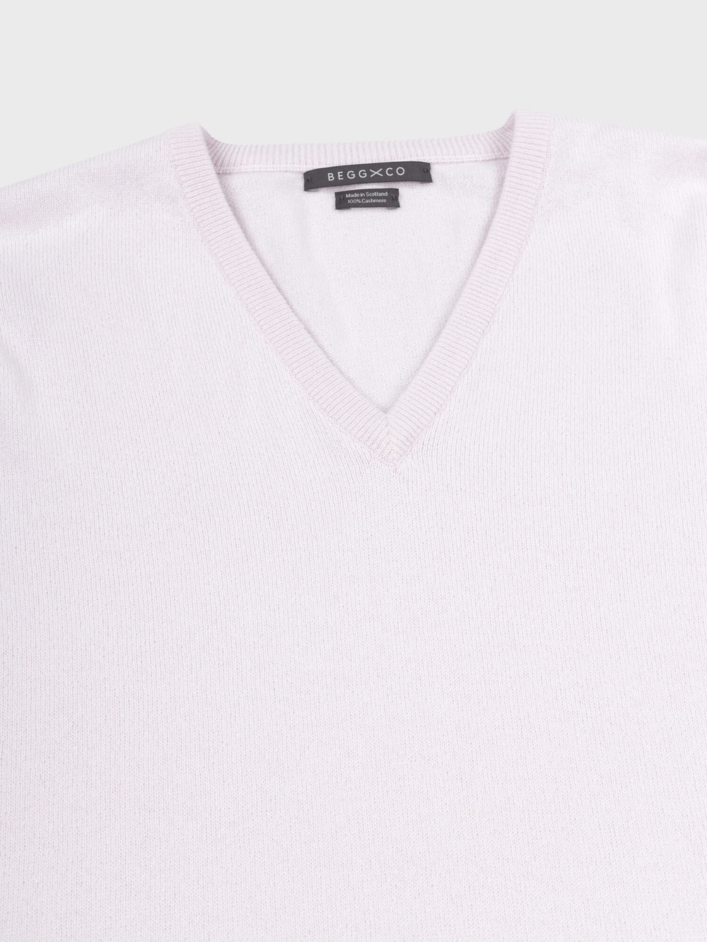 detail of a light pink cashmere v-neck sweater on a grey background