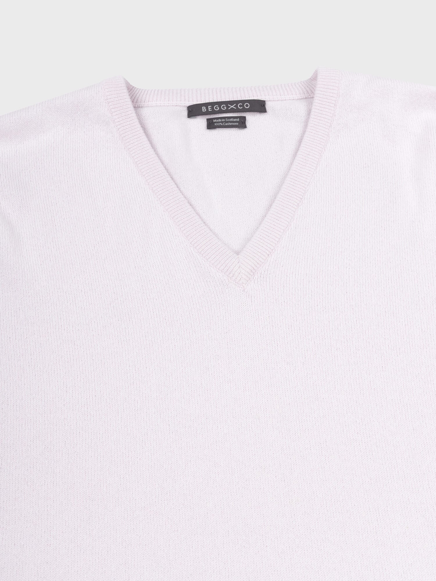 detail of a light pink cashmere v-neck sweater on a grey background