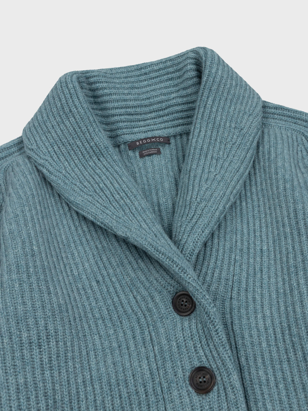 chunky ribbed green cashmere shawl collar cardigan neck detail with horn buttons on a grey background