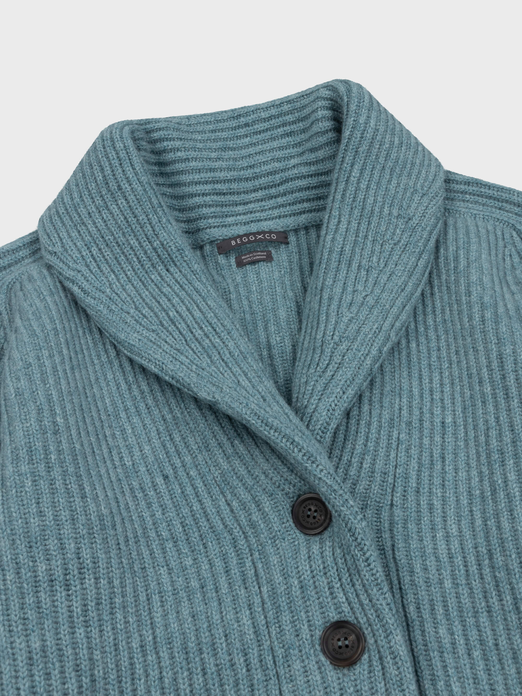 chunky ribbed green cashmere shawl collar cardigan neck detail with horn buttons on a grey background