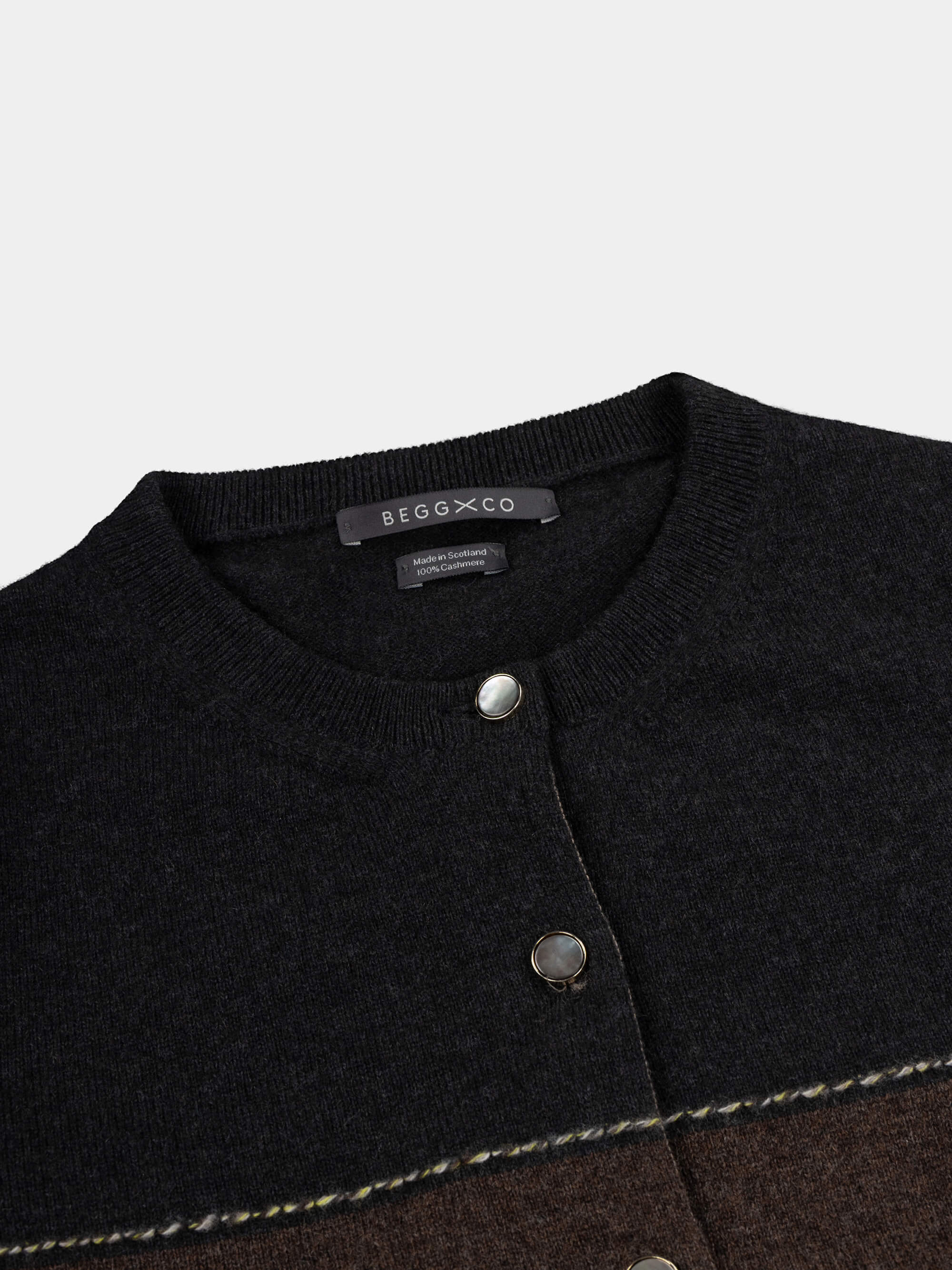 Close-up of a black and brown cardigan with 'Begg x Co' branding on a light gray background.