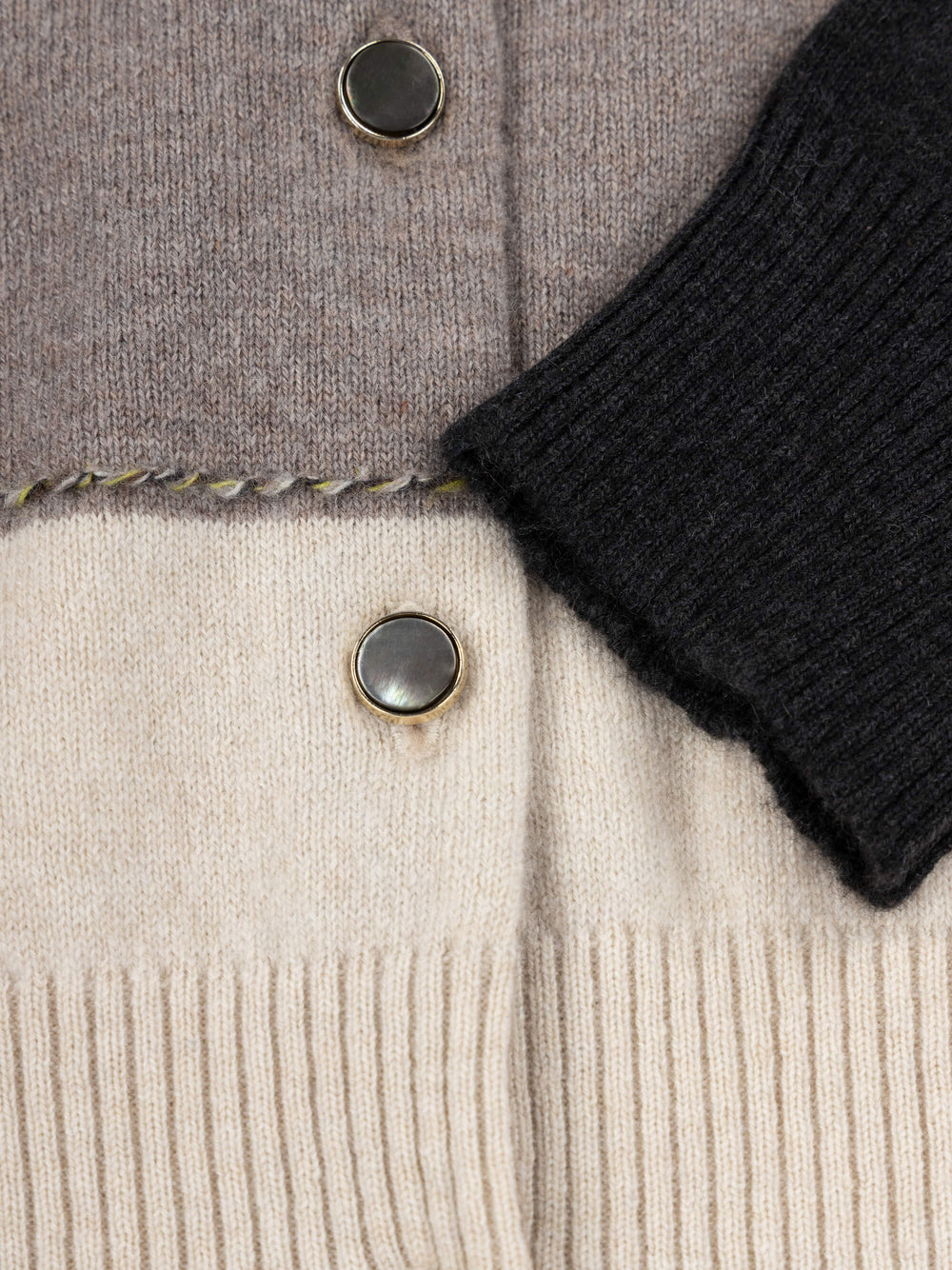 Close-up of a cashmere cardigan with buttons and a black sleeve.