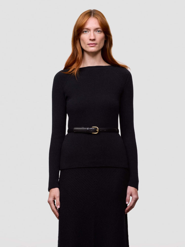 Woman wearing a black long-sleeve ribbed cashmere sweater and black skirt on a light gray background