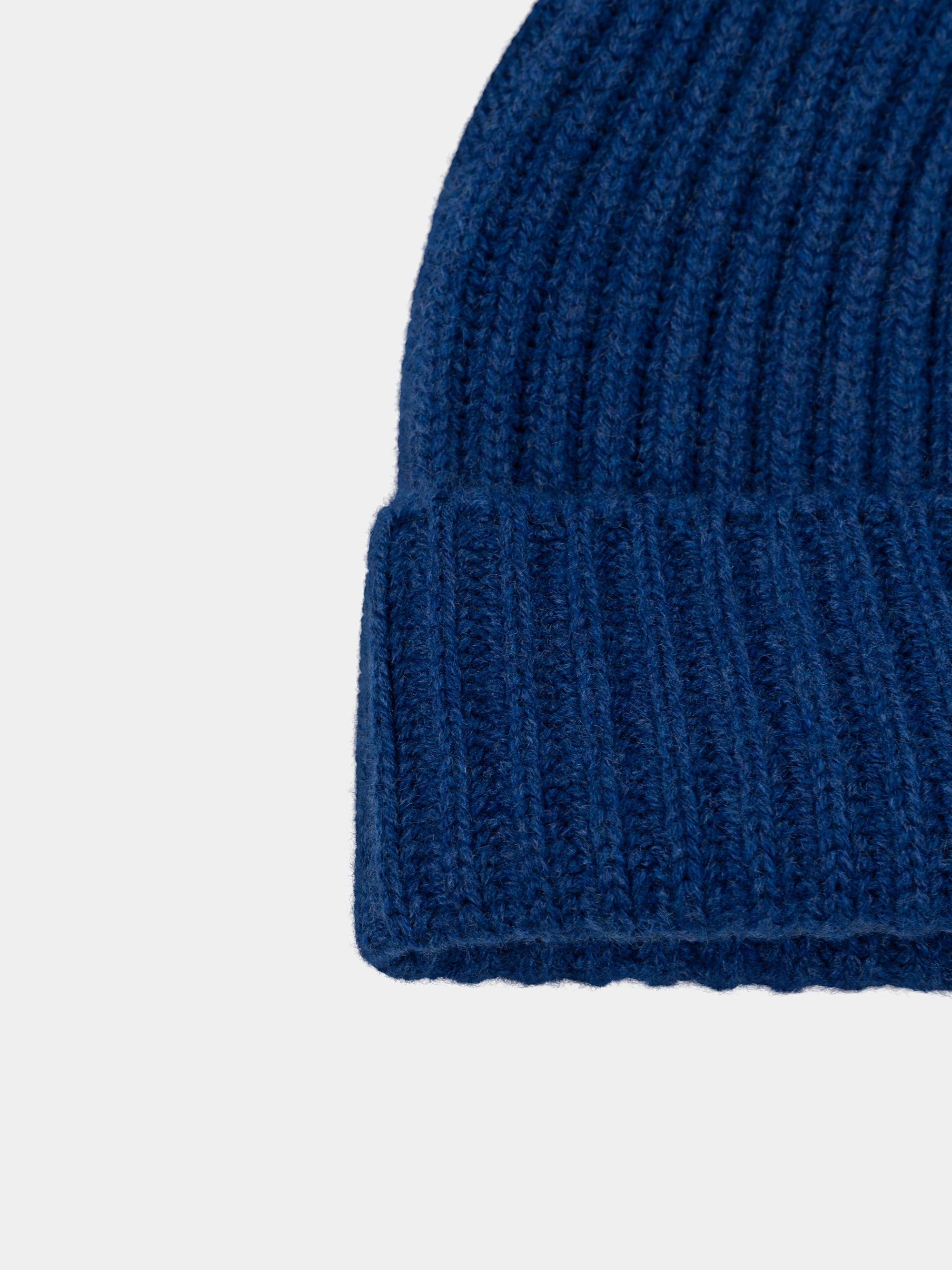 Close-up of a blue knitted cashmere beanie on a light gray background