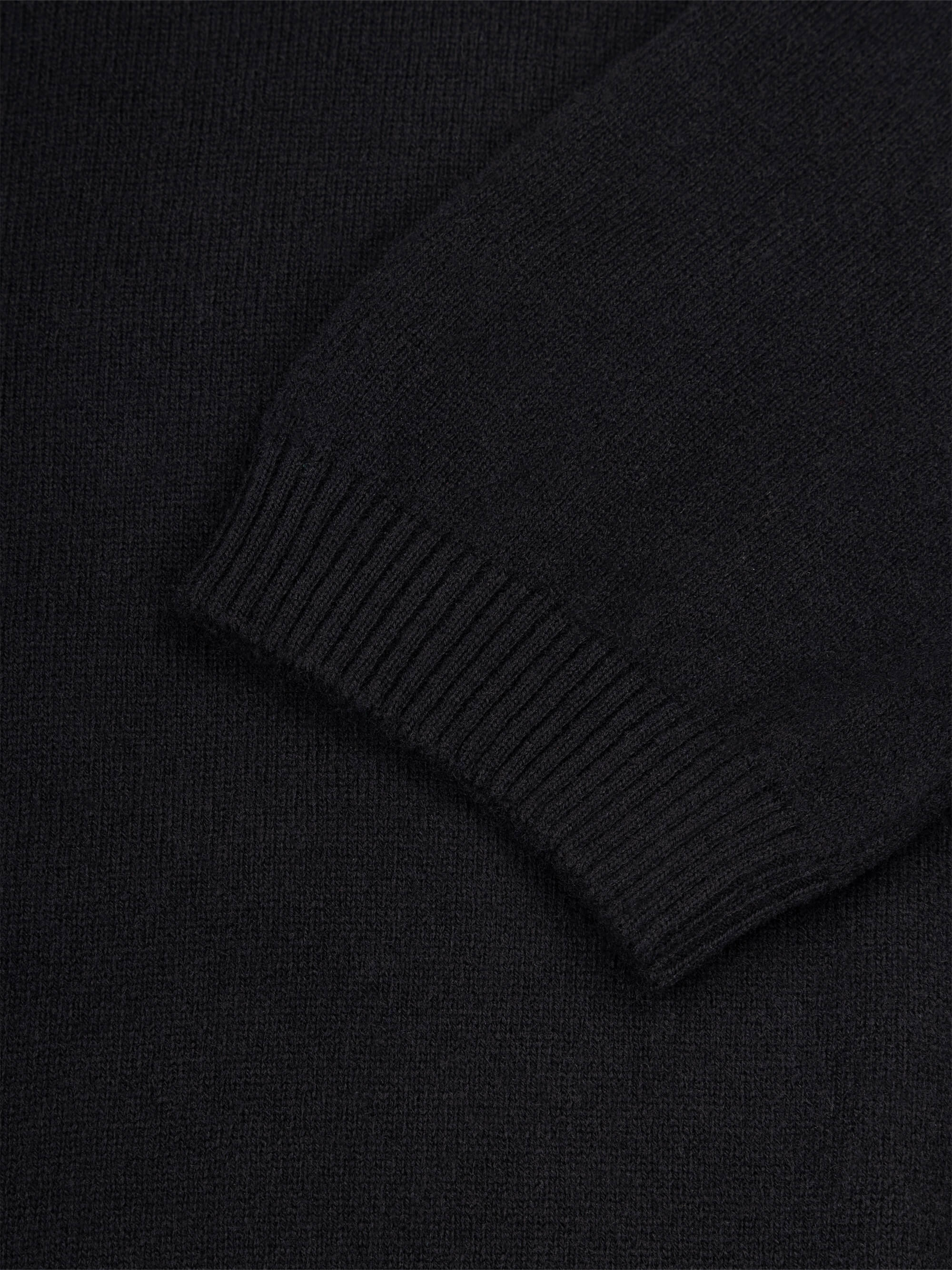 Close-up of a black cashmere t-shirt sleeve with ribbed texture.