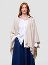 Woman wearing a beige poncho over a white shirt and blue pants on a plain background