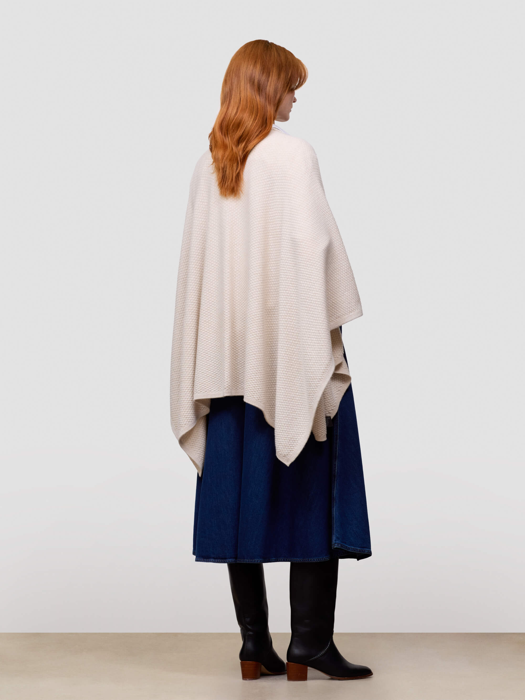 Woman wearing a beige poncho over a blue dress on a white background