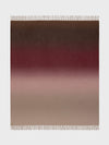 A Nuance Ombre throw blanket with a gradient of colors ranging from beige to red, featuring a subtle blend of shades with fringe detailing on the edges.