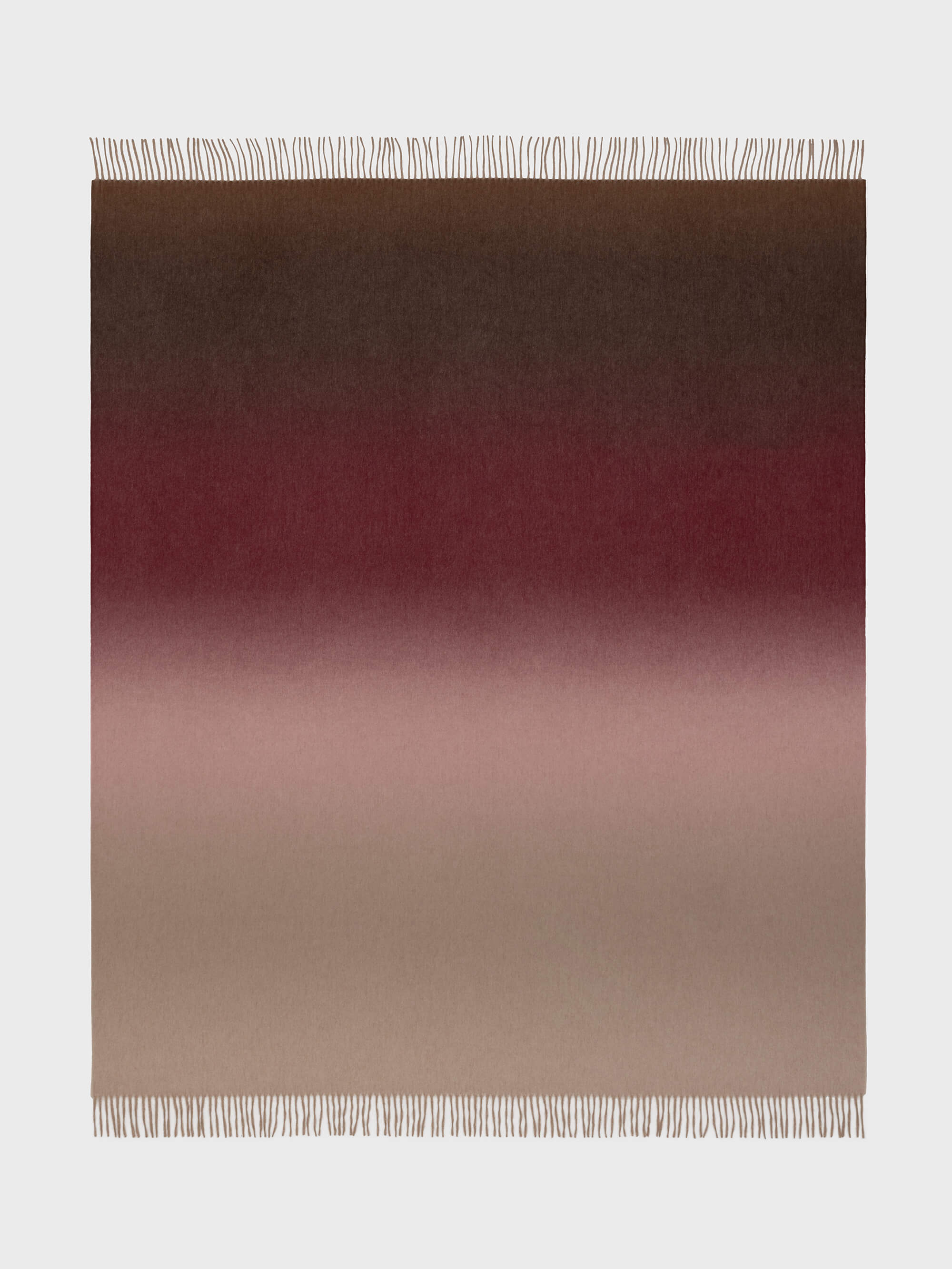 A Nuance Ombre throw blanket with a gradient of colors ranging from beige to red, featuring a subtle blend of shades with fringe detailing on the edges.