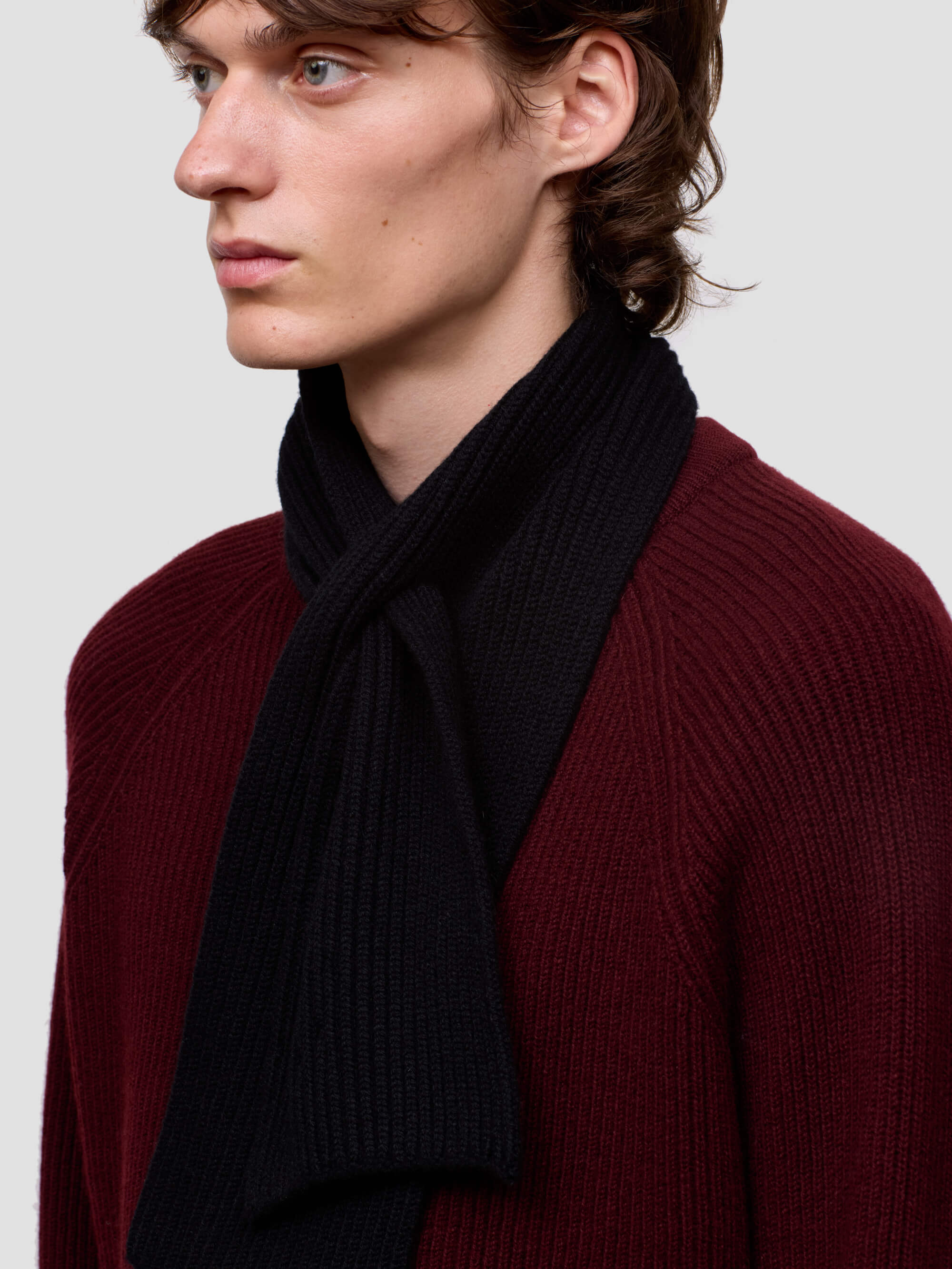 Person wearing a dark scarf and burgundy sweater against a plain background