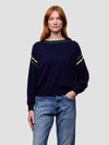 Woman wearing a navy sweater with green and yellow accents and blue jeans on a light gray background