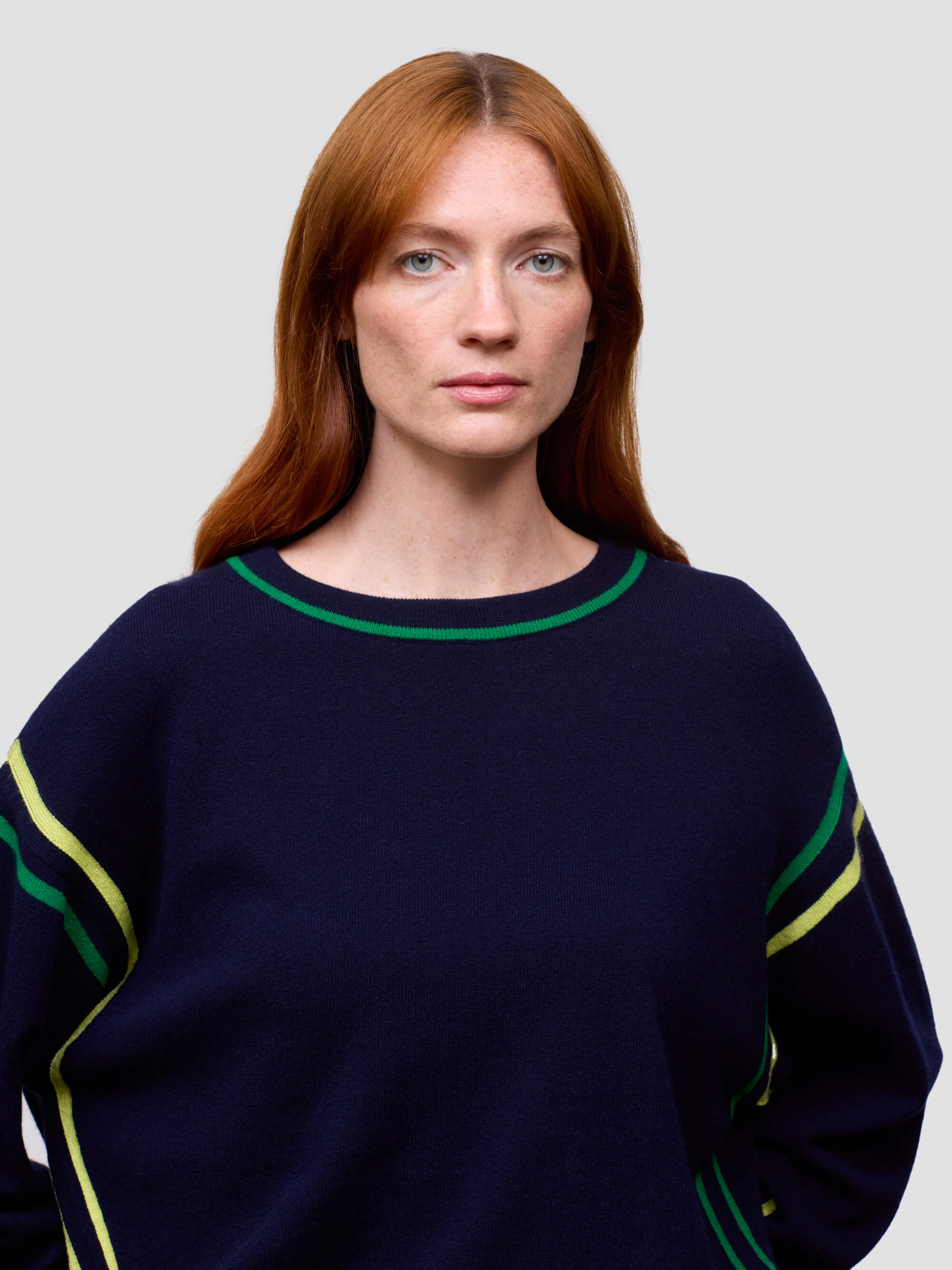 Woman wearing a navy sweater with green and yellow accents on a plain background