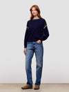 women wearing a navy sweater with green accents and blue jeans on a plain background