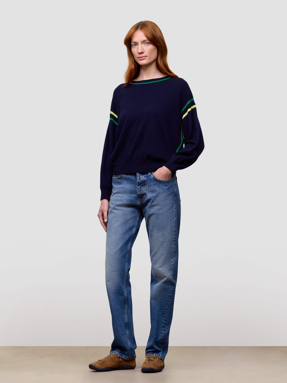 women wearing a navy sweater with green accents and blue jeans on a plain background