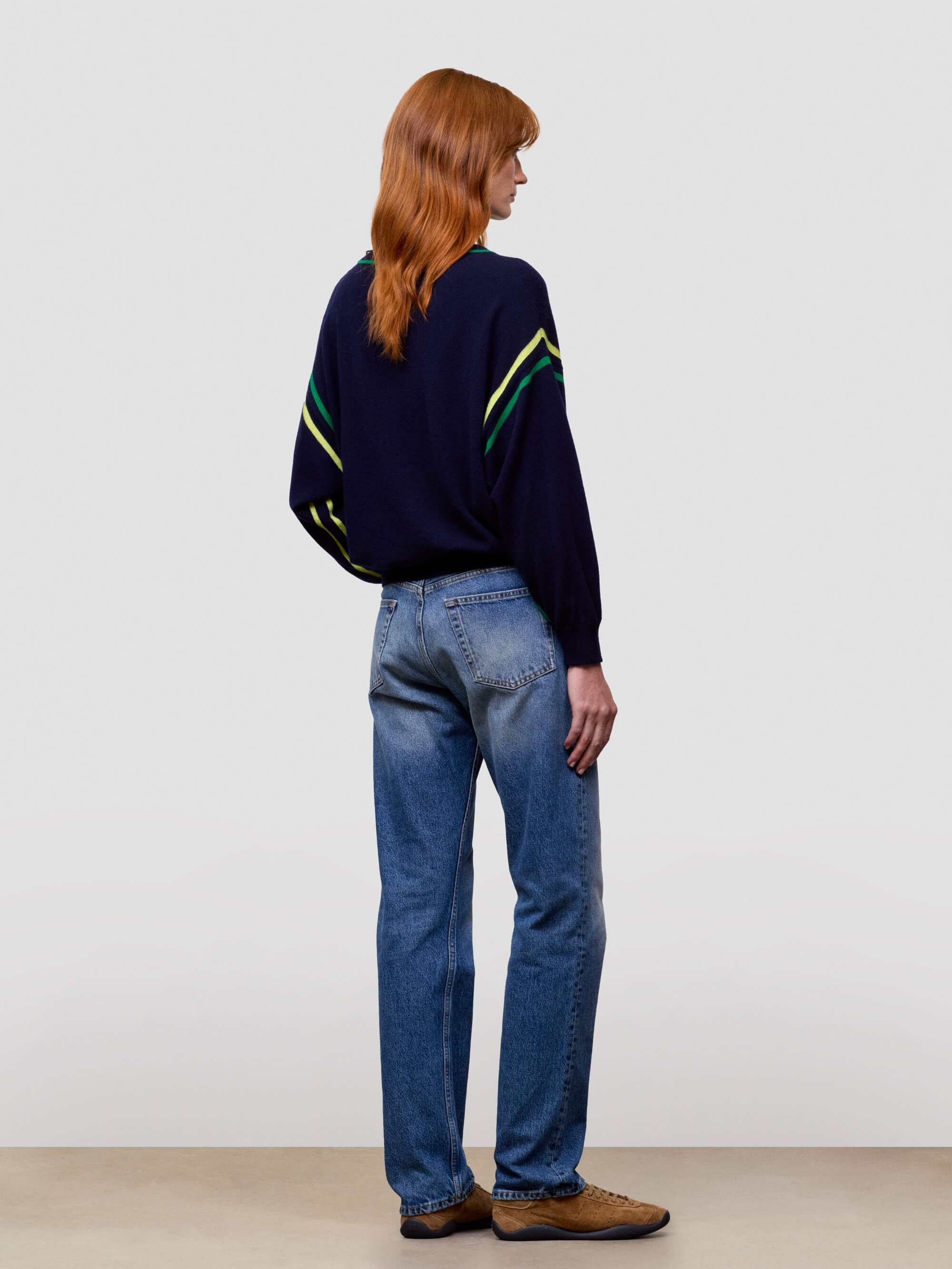women wearing a dark blue sweater with green and yellow accents and blue jeans on a plain background