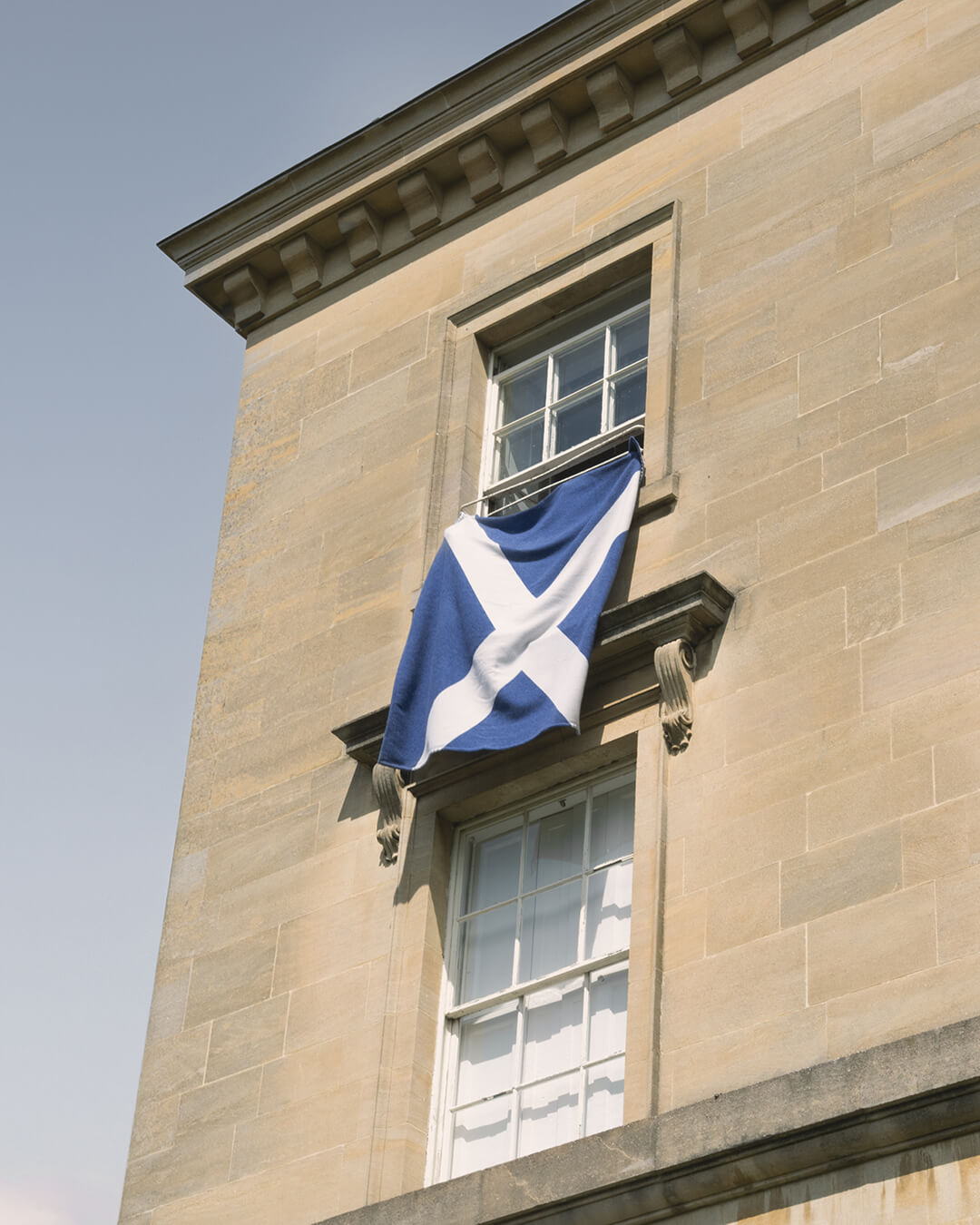 a blanket with scottish saltire design hanging out top window of a stone building