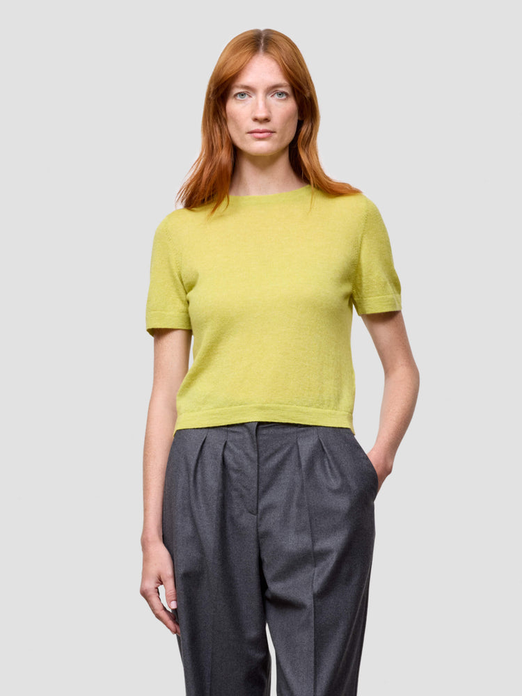 Woman wearing a yellow cashmere tshirt and gray pants against a light gray background