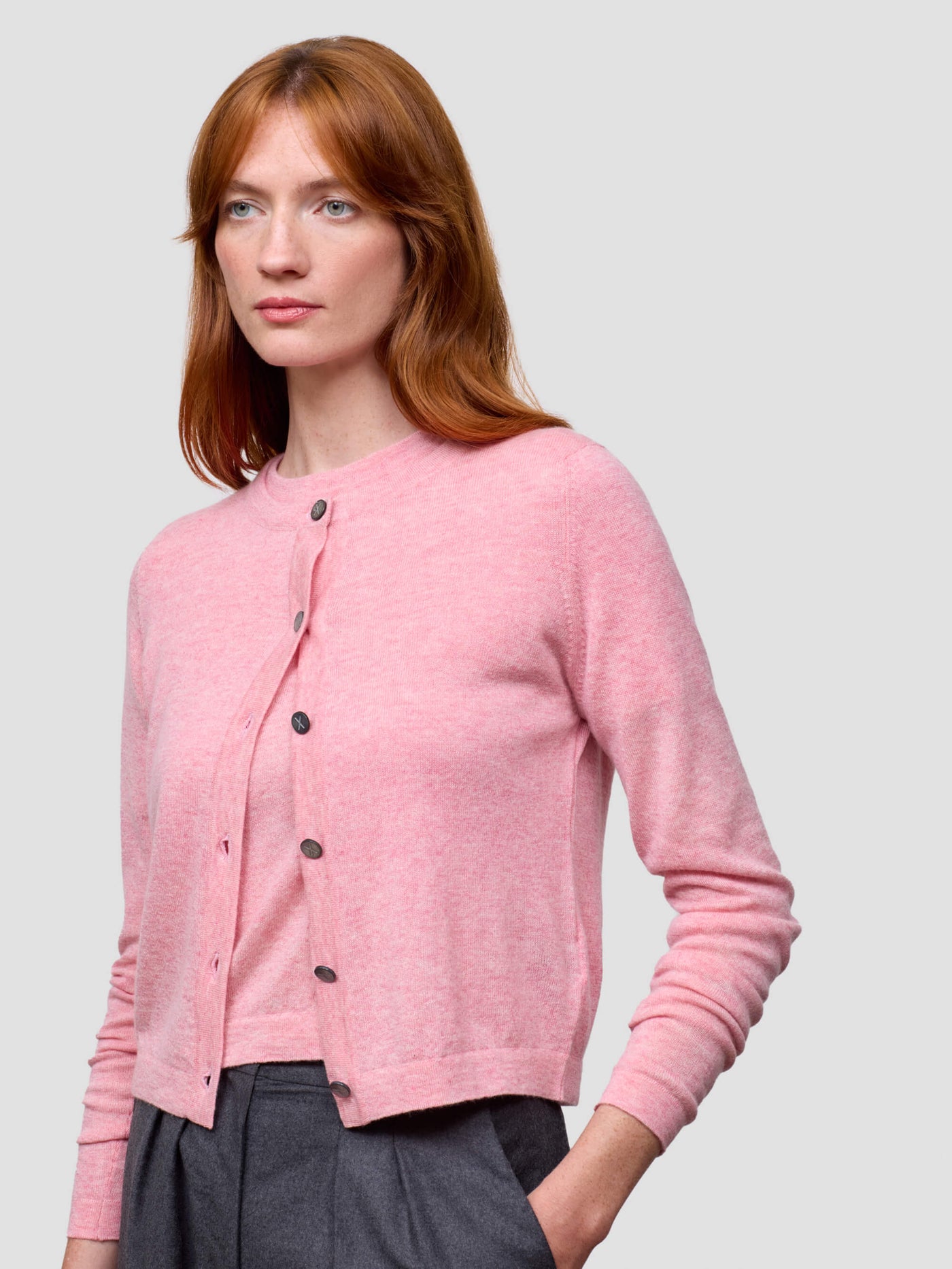 Woman wearing a pink cardigan with black buttons on a light gray background
