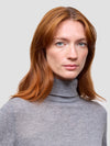 Woman wearing a gray turtleneck sweater against a light gray background