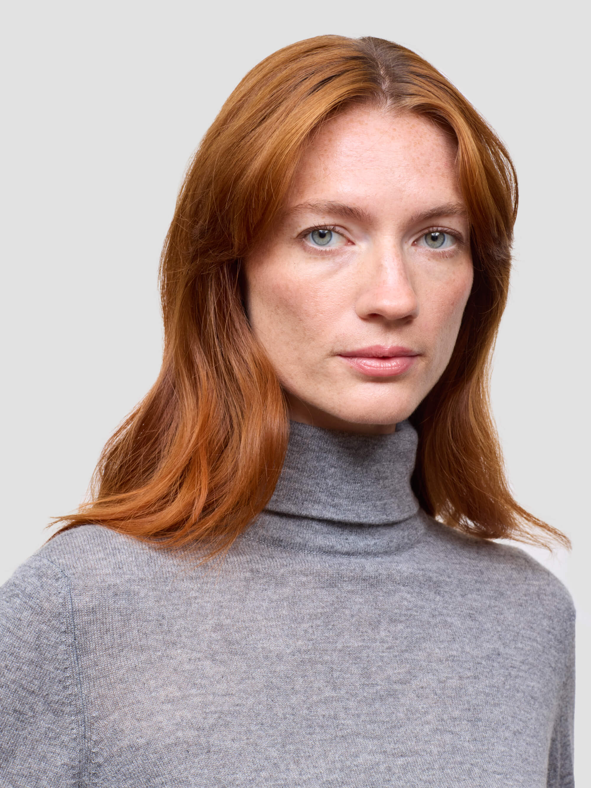 Woman wearing a gray turtleneck sweater against a light gray background
